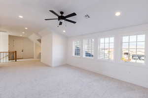 Carpeted spare room featuring ceiling fan, a healthy amount of sunlight, and vaulted ceiling