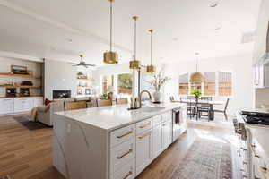 Kitchen featuring pendant lighting, a large fireplace, white cabinetry, and sink