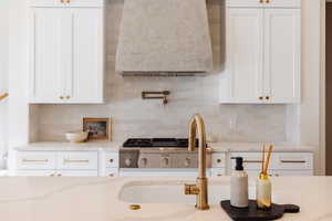 Kitchen featuring light stone countertops, backsplash, and white cabinetry