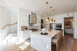 Kitchen with light stone countertops, wall chimney exhaust hood, backsplash, a spacious island, and appliances with stainless steel finishes