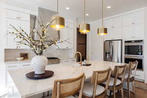 Kitchen with a kitchen island with sink, stainless steel fridge with ice dispenser, sink, and double oven