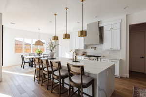 Kitchen featuring white cabinets, wall chimney exhaust hood, and hanging light fixtures