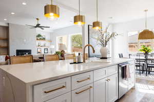 Kitchen with light stone counters, a large fireplace, sink, white cabinetry, and hanging light fixtures