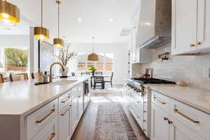 Kitchen featuring light stone countertops, stainless steel appliances, wall chimney range hood, decorative light fixtures, and white cabinetry