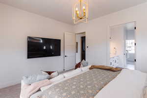 Bedroom with light carpet, ensuite bath, and a notable chandelier