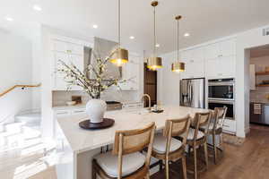 Kitchen with stainless steel fridge, light stone counters, backsplash, and an island with sink