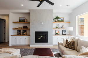 Living room featuring wood-type flooring, a large fireplace, ceiling fan, and a healthy amount of sunlight