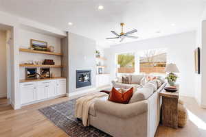 Living room featuring built in shelves, ceiling fan, light hardwood / wood-style floors, and a wood stove