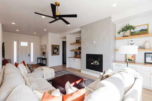 Living room with a fireplace, light wood-type flooring, and ceiling fan