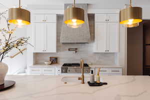 Kitchen featuring tasteful backsplash, light stone counters, white cabinetry, and hanging light fixtures