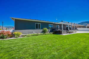 Rear view of house featuring a lawn, a mountain view, a patio area, and a hot tub