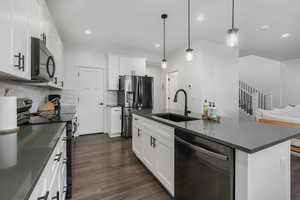 Kitchen with a center island with sink, white cabinets, decorative light fixtures, and stainless steel appliances.