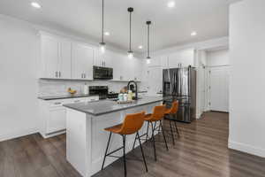 Kitchen featuring white cabinetry, hanging light fixtures, and appliances with stainless steel finishes.