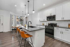 Kitchen featuring white cabinets, appliances with stainless steel finishes, a kitchen island with sink.