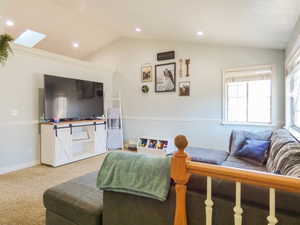 Carpeted living room featuring lofted ceiling with skylight