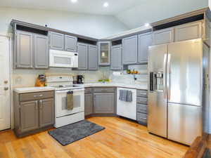 Kitchen featuring tasteful backsplash, white appliances, sink, light hardwood / wood-style floors, and lofted ceiling