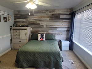 Carpeted bedroom featuring ceiling fan, wood walls, and crown molding