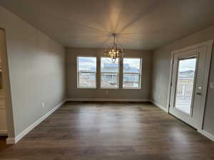 Unfurnished dining area featuring a textured ceiling, dark wood-type flooring, and an inviting chandelier