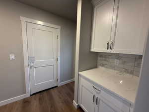 Bar with light stone counters, white cabinetry, dark wood-type flooring, and tasteful backsplash