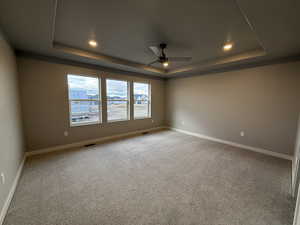 Spare room featuring a raised ceiling, ceiling fan, and carpet floors