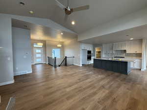 Kitchen with decorative backsplash, a kitchen island with sink, decorative light fixtures, white cabinets, and lofted ceiling