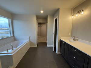 Bathroom featuring tile patterned floors, vanity, and a relaxing tiled tub