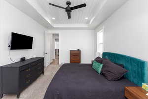 Carpeted bedroom with a tray ceiling, ceiling fan, and wooden ceiling