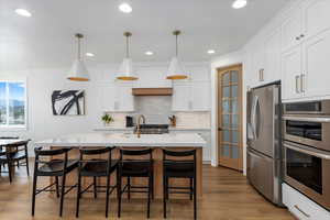 Kitchen featuring pendant lighting, decorative backsplash, an island with sink, appliances with stainless steel finishes, and white cabinetry