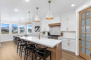 Kitchen featuring stove, a center island with sink, sink, hanging light fixtures, and white cabinetry