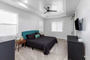 Bedroom featuring ceiling fan, a barn door, light colored carpet, a tray ceiling, and wood ceiling