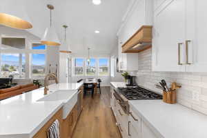 Kitchen with pendant lighting, light stone countertops, an island with sink, white cabinetry, and gas cooktop