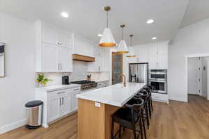 Kitchen with pendant lighting, white cabinets, a center island with sink, tasteful backsplash, and stainless steel appliances