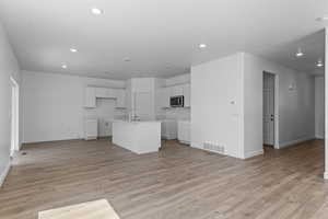 Kitchen featuring white cabinets, sink, light wood-type flooring, and an island with sink