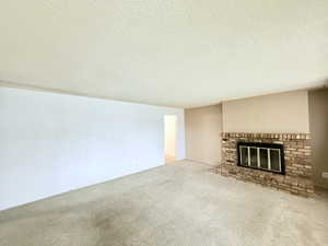 Unfurnished living room with a brick fireplace, a textured ceiling, and carpet floors