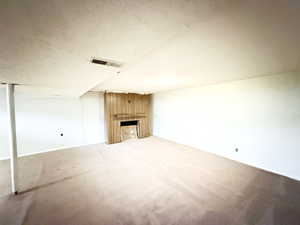 Unfurnished living room with a large fireplace, a textured ceiling, and carpet flooring