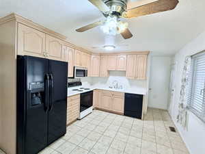 Kitchen with black appliances, light tile patterned floors, light brown cabinetry, and sink