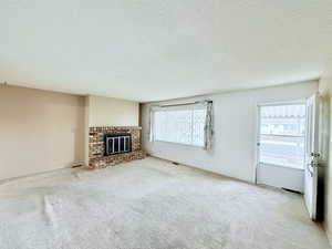 Unfurnished living room featuring plenty of natural light, a textured ceiling, light carpet, and a fireplace