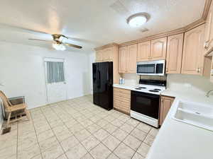 Kitchen with a textured ceiling, light brown cabinetry, sink, black fridge, and range with electric cooktop