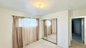 Unfurnished bedroom with light colored carpet, a closet, and a textured ceiling