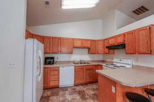 Kitchen featuring kitchen peninsula, lofted ceiling, a breakfast bar, sink, and white appliances