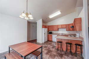 Kitchen featuring a notable chandelier, white appliances, lofted ceiling, sink, and kitchen peninsula