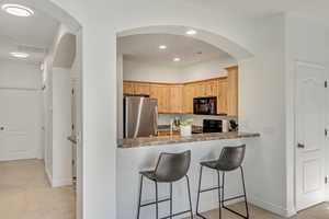 Kitchen featuring light brown cabinets, black appliances, light colored carpet, kitchen peninsula, and a breakfast bar area