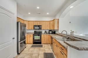 Kitchen with light brown cabinetry, kitchen peninsula, sink, and black appliances