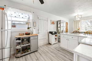 Kitchen with ceiling fan with notable chandelier, a textured ceiling, white refrigerator, light hardwood / wood-style floors, and white cabinetry