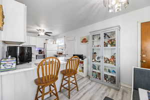 Kitchen with white cabinetry, ceiling fan, white fridge, light hardwood / wood-style floors, and a breakfast bar area