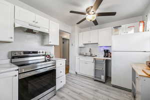 Kitchen featuring stainless steel electric range oven, sink, white refrigerator, white cabinets, and light wood-type flooring