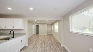 Kitchen with light stone countertops, sink, white cabinets, and light hardwood / wood-style flooring