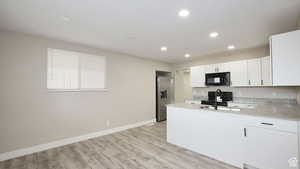 Kitchen with black appliances, light stone countertops, white cabinetry, and light wood-type flooring