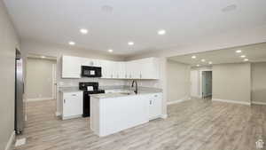 Kitchen with white cabinetry, sink, black appliances, and light hardwood / wood-style flooring