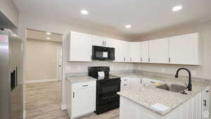 Kitchen featuring black appliances, white cabinets, light stone countertops, and sink